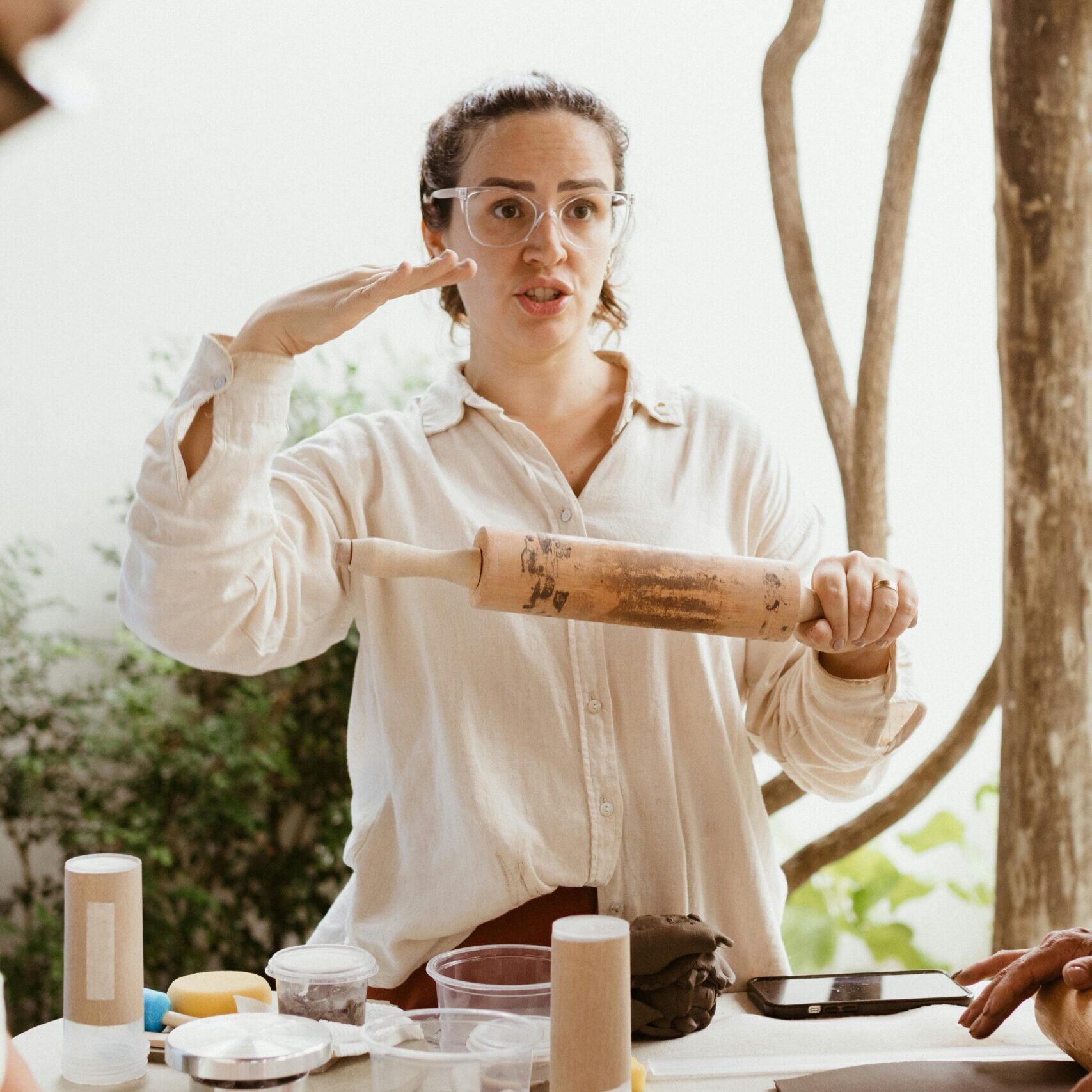 A woman with a rolling pin stands poised to lead a skills-based cooking workshop, emphasizing practical culinary techniques.