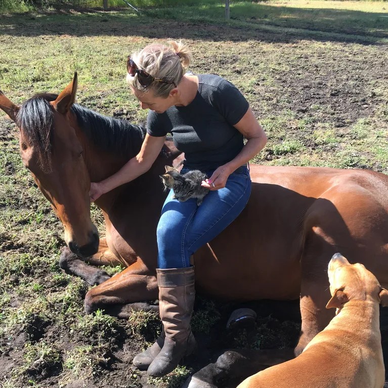 Amanda Berry gently pets a horse while sitting on the ground. Equine therapy is part of Follow Through House's rehab & skill development programs.