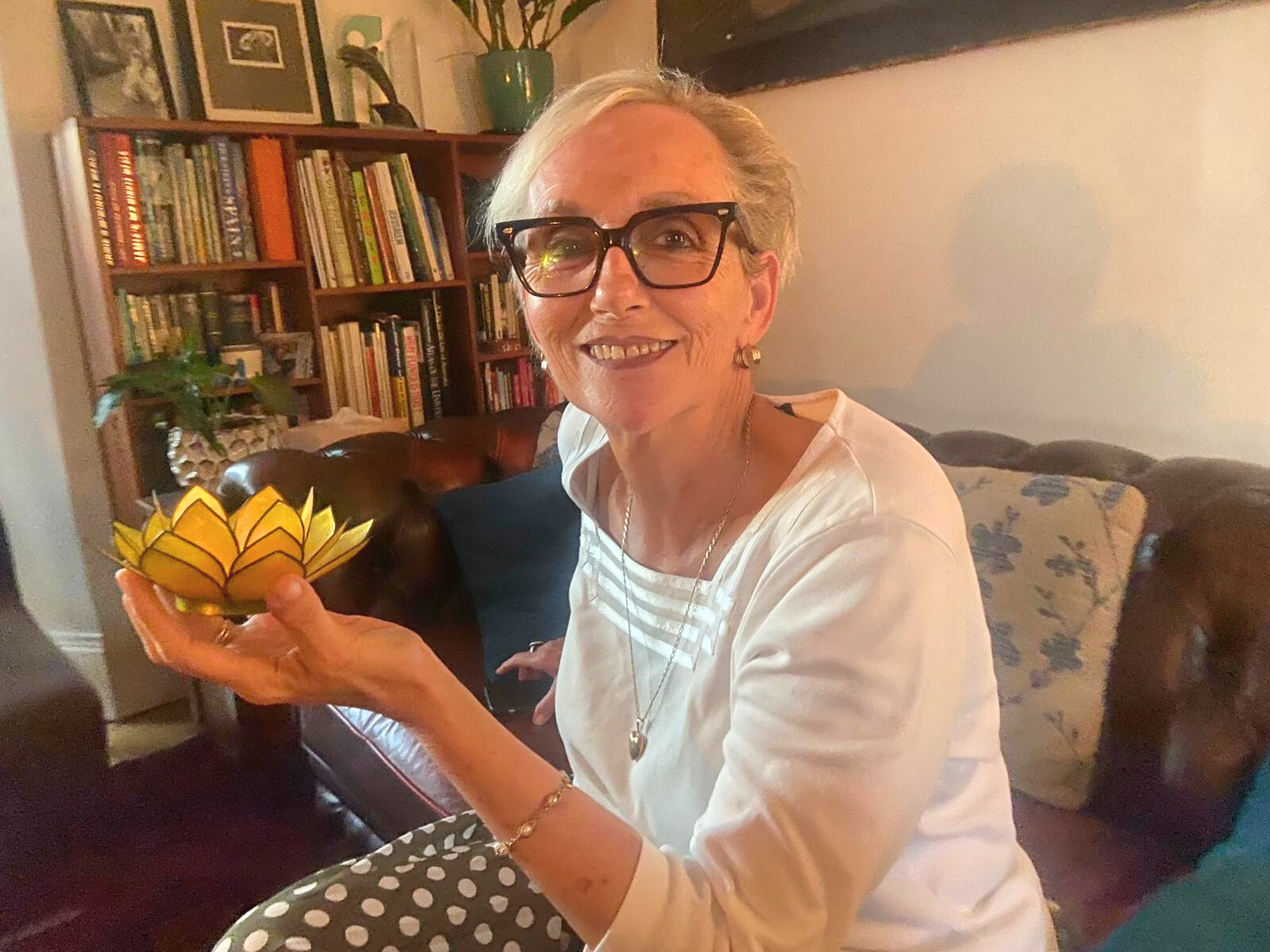 Joanna Macdougall, CEO of Follow Though House, is depicted wearing glasses and holding a bright yellow flower. Joanna Macdougall, CEO of Follow Though House, is depicted wearing glasses and holding a bright yellow flower.
